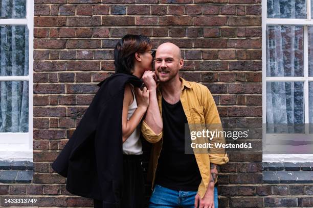 young man whispering boyfriend's ear in front of building - confidential palabra en inglés fotografías e imágenes de stock