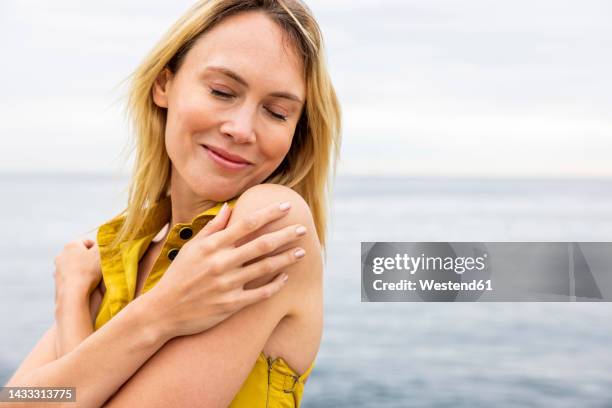 smiling woman with eyes closed hugging self - hugging self stock-fotos und bilder