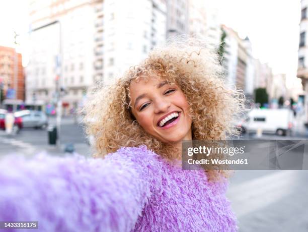 happy woman with blond afro hairstyle taking selfie in city - blonde woman selfie stock pictures, royalty-free photos & images