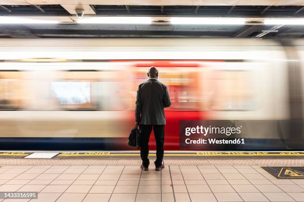 senior passenger with laptop bag standing in front of speeding train on subway platform - london underground stockfoto's en -beelden