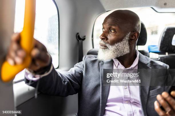 senior businessman holding handle and looking through taxi window - london taxi stock-fotos und bilder