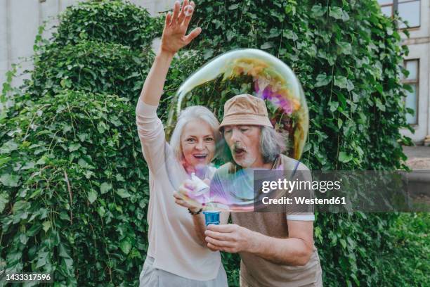 happy mature woman enjoying by senior man making bubbles in park - bubbles happy stockfoto's en -beelden