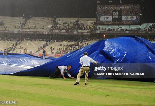 Indian groundsmen run to cover the pitch whilst an official falls as the IPL Twenty20 cricket match between Deccan Chargers and Kolkata Knight Riders...