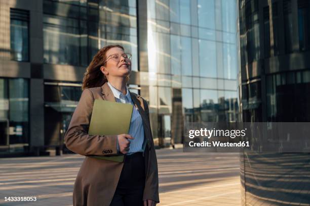 smiling businesswoman with eyes closed standing by office building - russian business woman stock-fotos und bilder