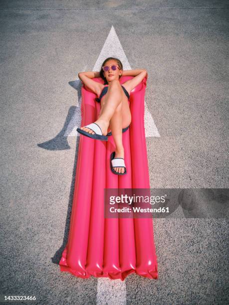 girl relaxing on inflatable pool raft in parking lot - luftmatraze stock-fotos und bilder