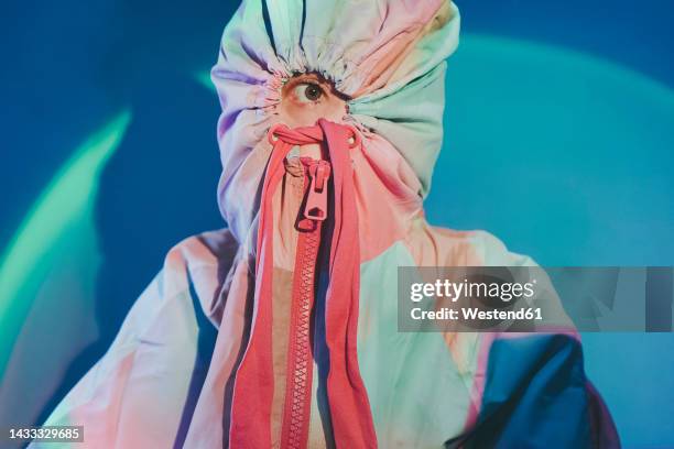 woman covering face with colorful hooded shirt in front of wall - hide stock-fotos und bilder