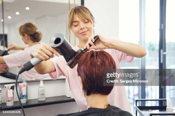 hairstylist working with client hairs with hairdryer - coiffeur stock-fotos und bilder