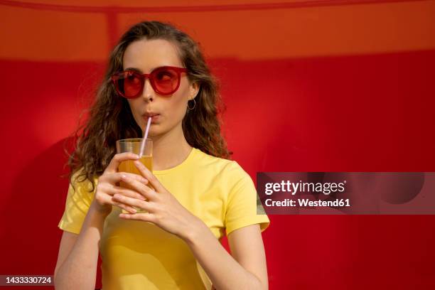 contemplative woman drinking juice in front of red wall - straw stock-fotos und bilder