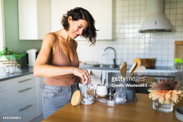 happy woman filling glass jar at kitchen counter - träsked bildbanksfoton och bilder