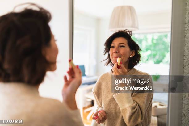 mature woman looking in mirror and applying lipstick - lipstick bildbanksfoton och bilder