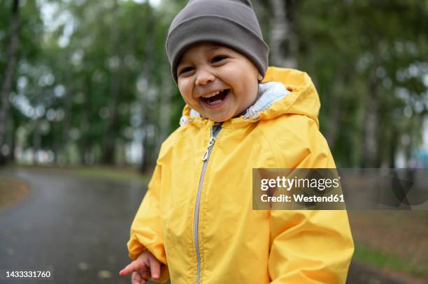 cute happy boy wearing knit hat and yellow rain jacket - happy toddler stockfoto's en -beelden