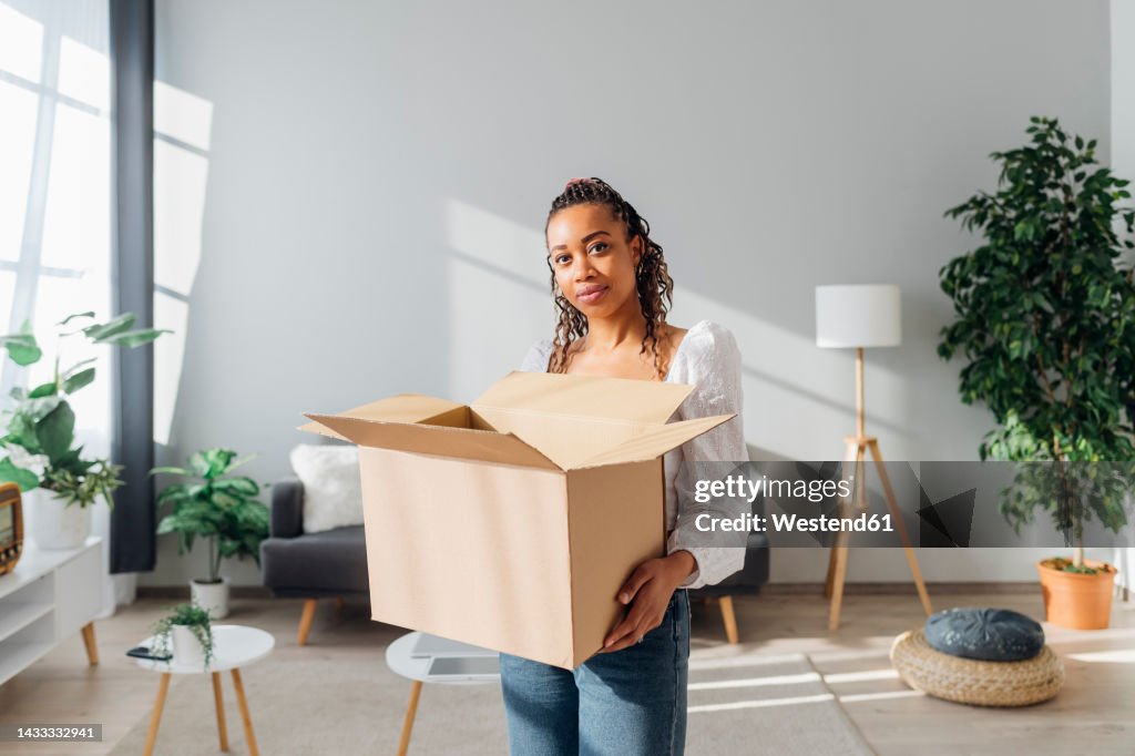 Young woman with cardboard box standing in new house