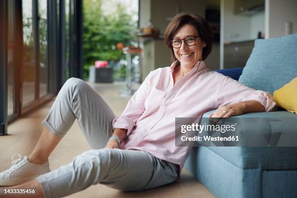 happy woman sitting on floor by sofa at home - westend61 fotografías e imágenes de stock