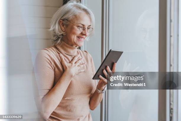 happy mature woman on video call through tablet pc at home - main sur la poitrine photos et images de collection
