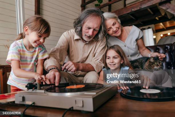 grandfather with granddaughters playing music on vinyl record player at home - lp fotografías e imágenes de stock