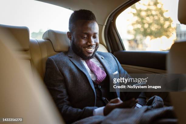 schwarzer geschäftsmann, der auf dem rücksitz der limousine sms schreibt - businessman taxi stock-fotos und bilder