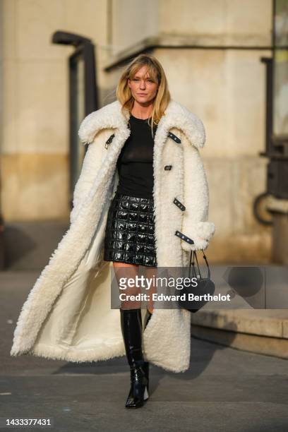 Jeanette Madsen wears a black t-shirt, a black shiny leather embossed checkered print pattern varnished short skirt, a white latte oversized fluffy...