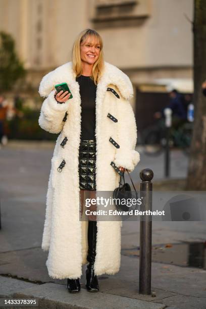 Jeanette Madsen wears a black t-shirt, a black shiny leather embossed checkered print pattern varnished short skirt, a white latte oversized fluffy...