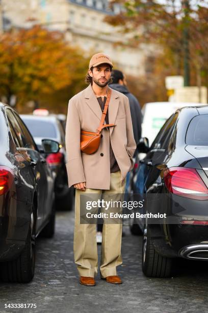 Rocques wears a brown sponge with embroidered brown logo cap from Lanvin, a white pearls necklace, a brown wool ribbed / buttoned cardigan, a beige...