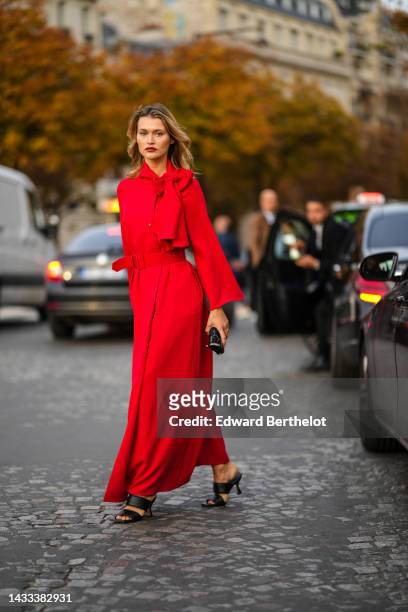 Chloe Lecareux wears a red flashy knot high neck / long sleeves / belted long dress, a black embroidered pattern circle clutch, black shiny leather...