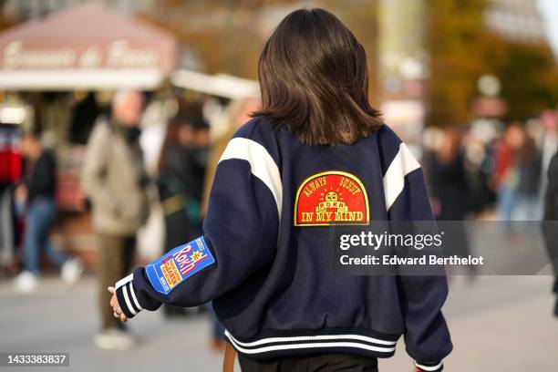 Mary Leest wears a navy blue felt with embroidered red / yellow / blue print pattern teddy coat, black large pants, outside Rokh, Paris Fashion Week...