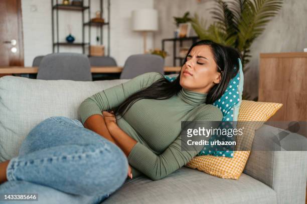 young woman having period cramps at home - dor de barriga imagens e fotografias de stock