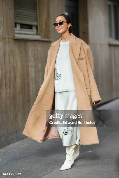 Chriselle Lim wears black sunglasses, silver earrings, a white with embroidered cut-out macrame pattern oversized pullover, a matching white with...