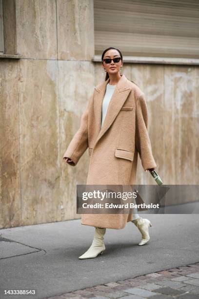 Chriselle Lim wears black sunglasses, silver earrings, a white with embroidered cut-out macrame pattern oversized pullover, a matching white with...