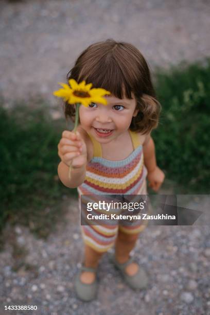 a colorful picture of a beautiful toddler girl in a striped suit with a yellow flower - colorful vegetables summer stock-fotos und bilder