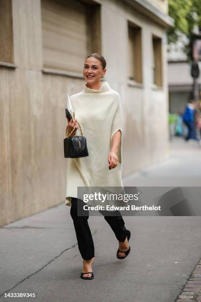 Sophia Roe wears gold and diamonds large earrings, a white latte wool ribbed high neck / sleeveless / oversized wool pullover, a black shiny leather...