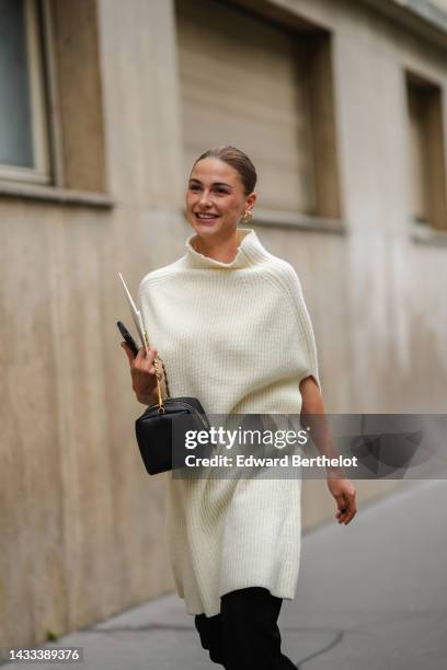 Sophia Roe wears gold and diamonds large earrings, a white latte wool ribbed high neck / sleeveless / oversized wool pullover, a black shiny leather...