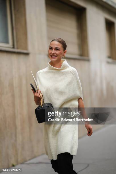 Sophia Roe wears gold and diamonds large earrings, a white latte wool ribbed high neck / sleeveless / oversized wool pullover, a black shiny leather...