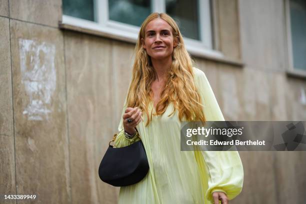 Blanca Miro wears a pale yellow long sleeves / V-neck / ruffled knees dress, a black fabric with gold panther handle handbag from Lanvin, a silver...