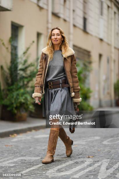 Alexandra Golovanoff wears a gray wool pullover, a gray pleated / accordion knees skirt, a brown leather and beige sheep interior jacket, brown shiny...