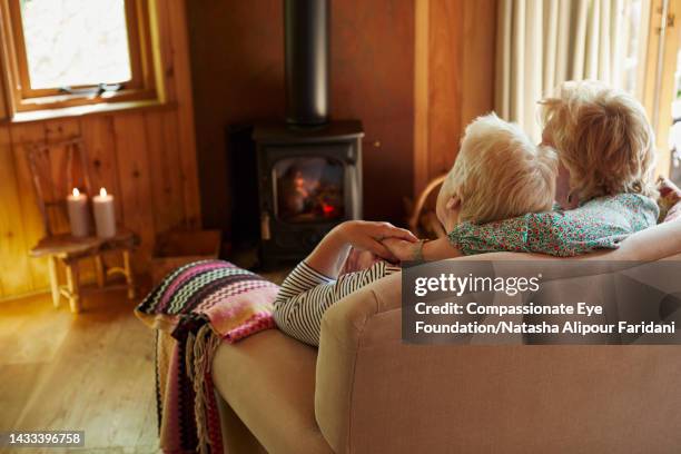 senior lesbian couple relaxing on sofa at log cabin - log cabin fire stock pictures, royalty-free photos & images