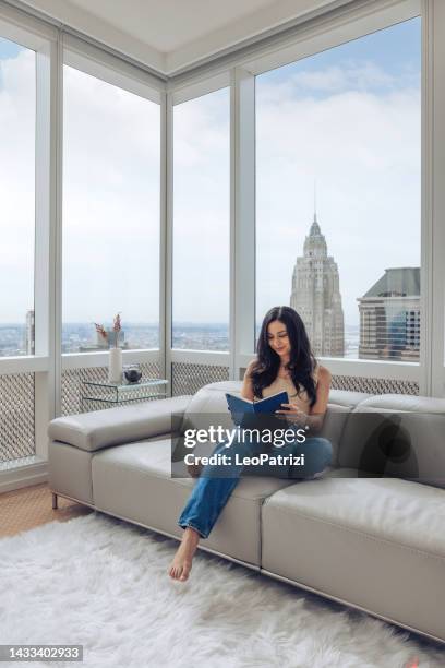 woman read a book sitting on the couch - day in life of a new yorker - women of penthouse stock pictures, royalty-free photos & images