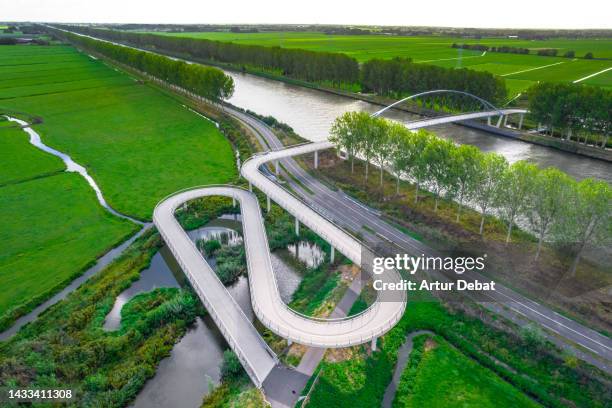 aerial view of beautiful bicycle lane ramp crossing river with green landscape in the netherlands. - riverbank stock pictures, royalty-free photos & images