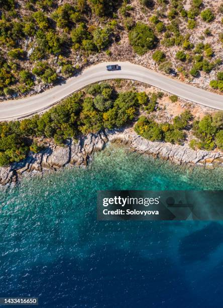 Aerial vertical shot of pickup truck moving by the curved road near sea tranquil waves on coast on Cephalonia Greek island. Transportation, traveling and nature concept.