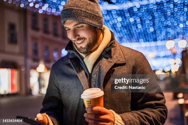 young man drinking coffee using smart phone on christmas day - winter coat stock pictures, royalty-free photos & images