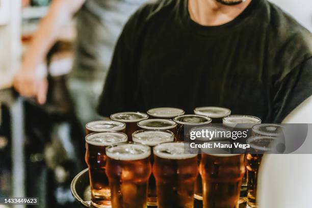 a waiter carrying several glasses of beer on a tray to serve customers. - busy pub stock pictures, royalty-free photos & images