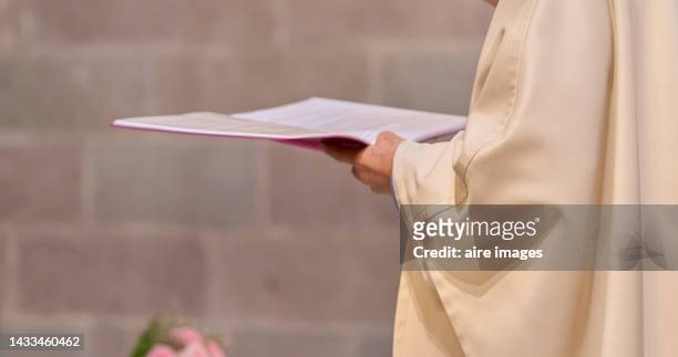 father in the catholic church with a book reading at mass his prayers to parishioners - cattolicesimo foto e immagini stock