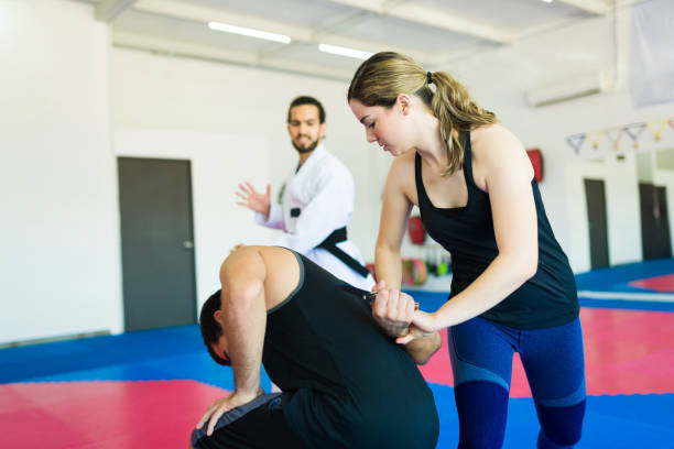 A woman practicing a self-defense technique on a male peer in a fitness class setting.