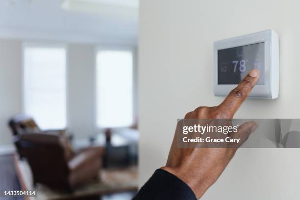 woman adjusts thermostat - thermostat fotografías e imágenes de stock