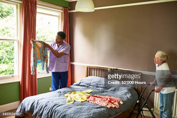 male care worker holding up cardigan for senior woman choosing what clothes to put on - get dressed male stock-fotos und bilder