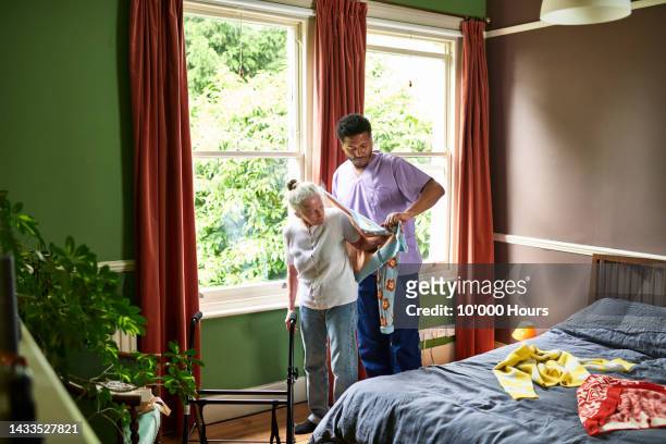 male care worker helping senior woman put on a cardigan - get dressed male stock-fotos und bilder