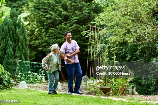 care worker and senior woman walking arm in arm in garden - hospice stock pictures, royalty-free photos & images