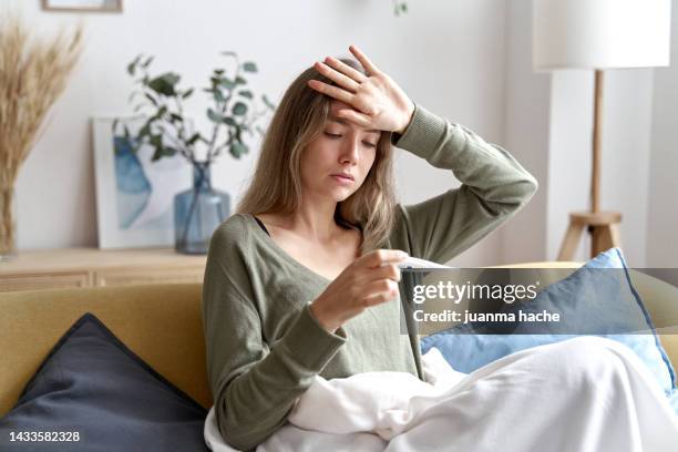 sick woman taking her temperature with a thermometer at home. - termometer bildbanksfoton och bilder