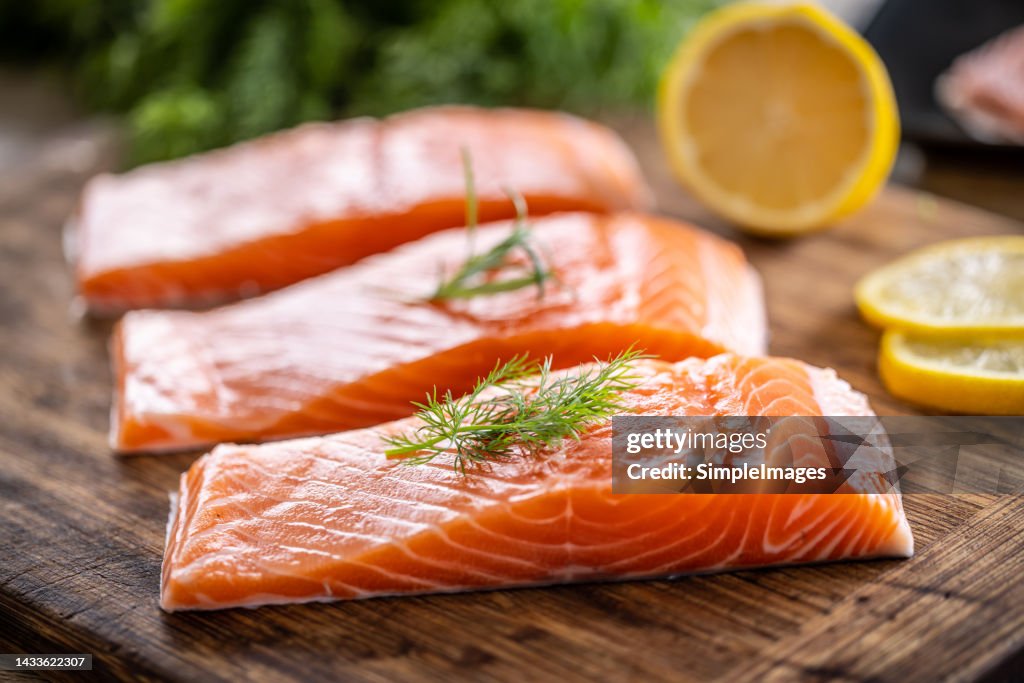 Raw salmon fillets onwooden cutting board with dill, rosemary and lemon.