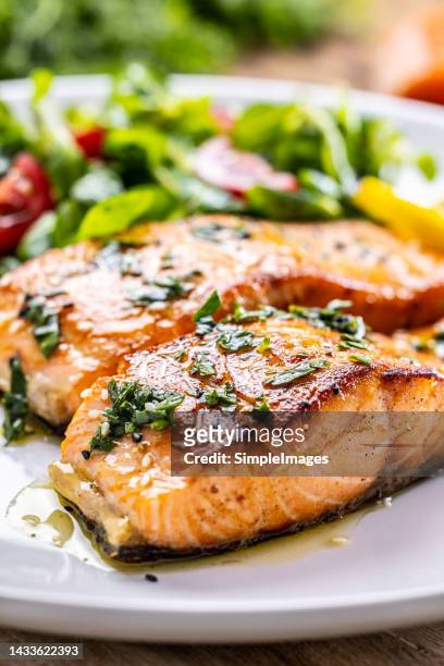 two salmon fillets baked until crispy with parsley herbs, as a side salad marinated with tomatoes. - salmon steak stock-fotos und bilder