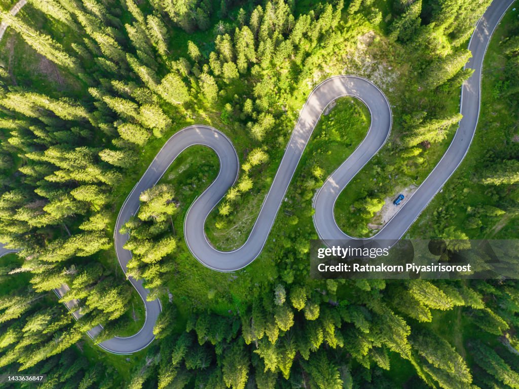 Aerial view of a road winding through a dense green forest in dolomites national park, Drone panoramic photo of the beautiful mountain pass hidden in the autumnn pine forest with the soft light of the autumn sunset, Dolomites Alps, South Tyrol, Italy